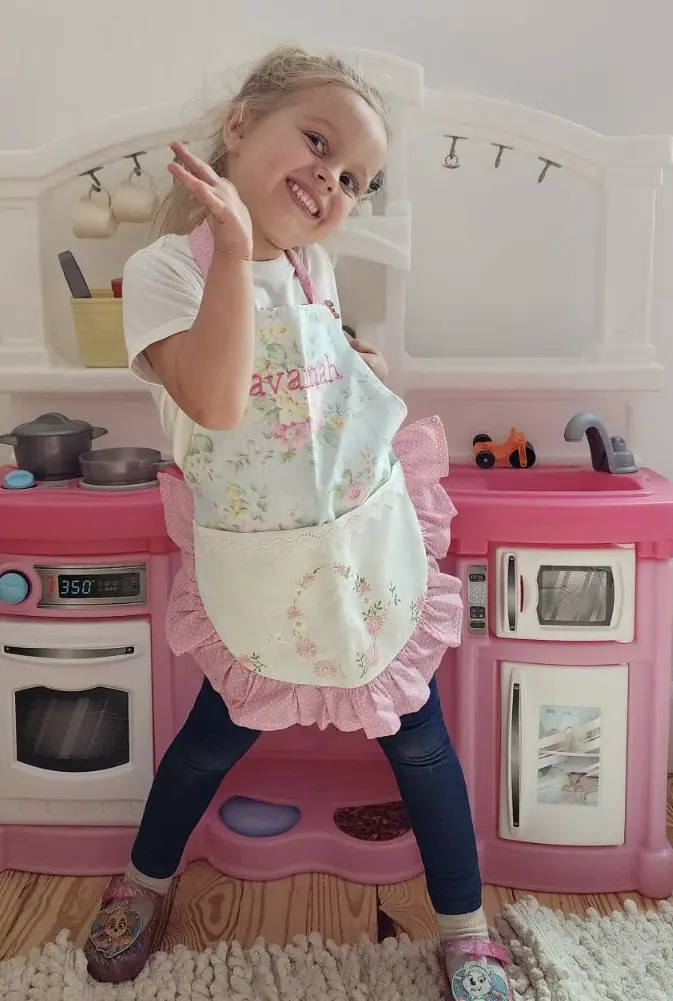 Child posing in front of toy kitchen.